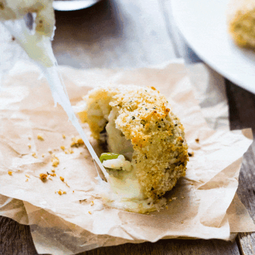 Leftover Risotto Cheesy Rice Balls (Arancini) served on a square of parchment paper and torn in half to show the stretchy cheese coming out
