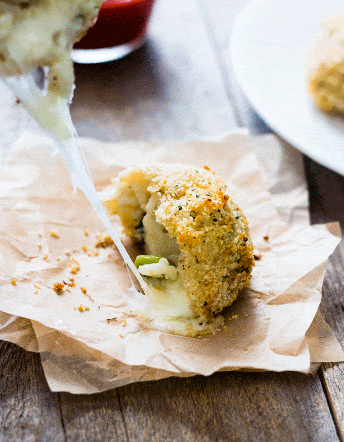 Leftover Risotto Cheesy Rice Balls (Arancini) served on a square of parchment paper and torn in half to show the stretchy cheese coming out