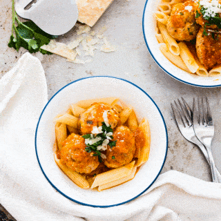 fresh tomato sauce on top of some meatballs and pasta in a white bowl and topped with grated cheese and basil