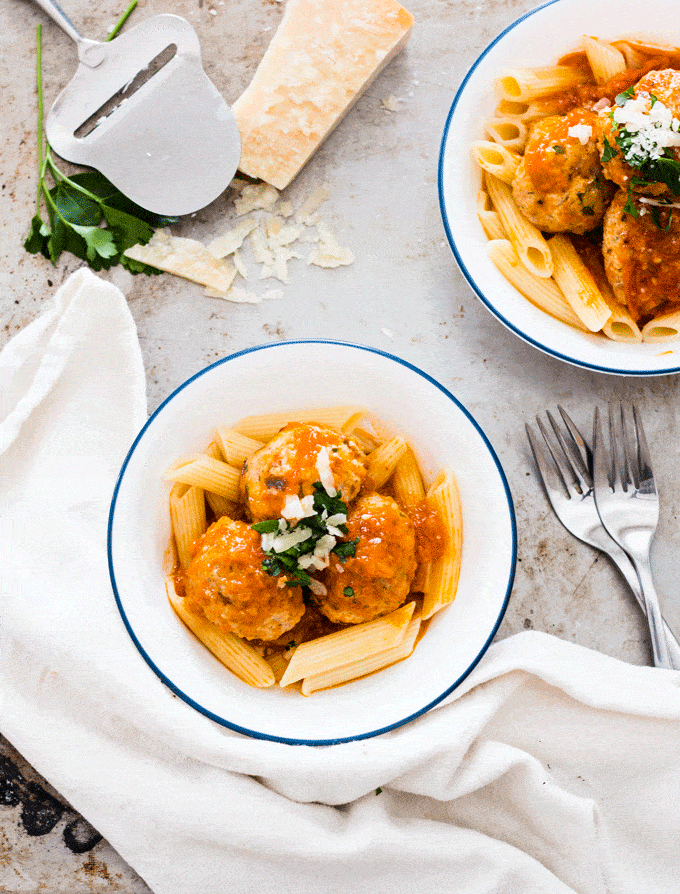 fresh tomato sauce on top of some meatballs and pasta in a white bowl and topped with grated cheese and basil