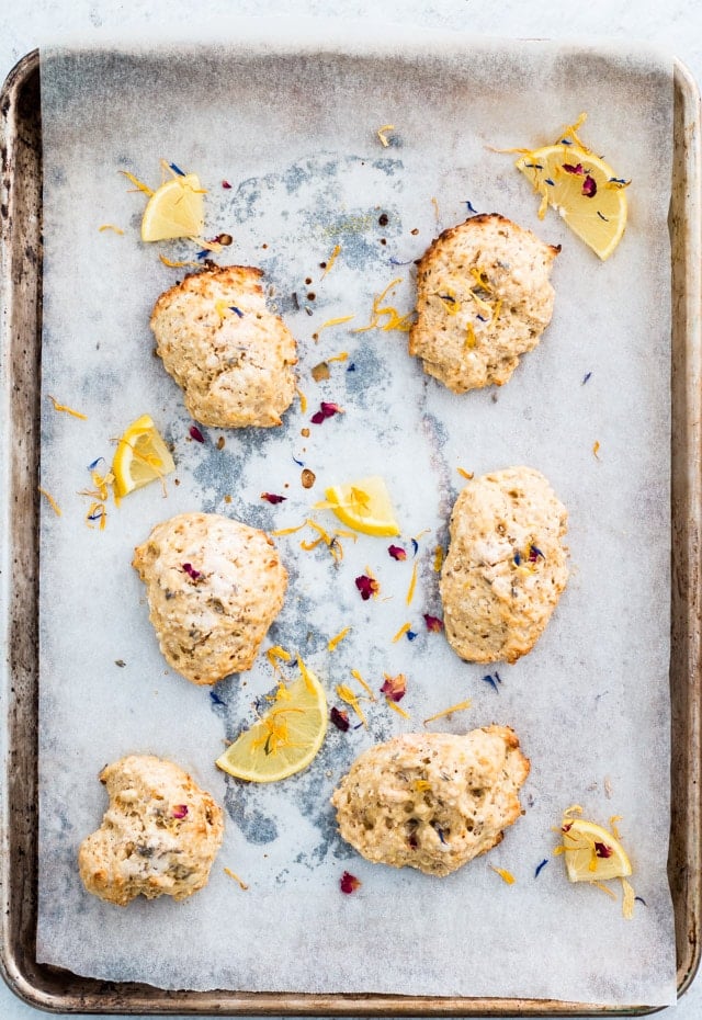 Overhead shot of 6 lemon and lavender scones on a baking tray and sprinkled with edible flowers and small lemon wedges