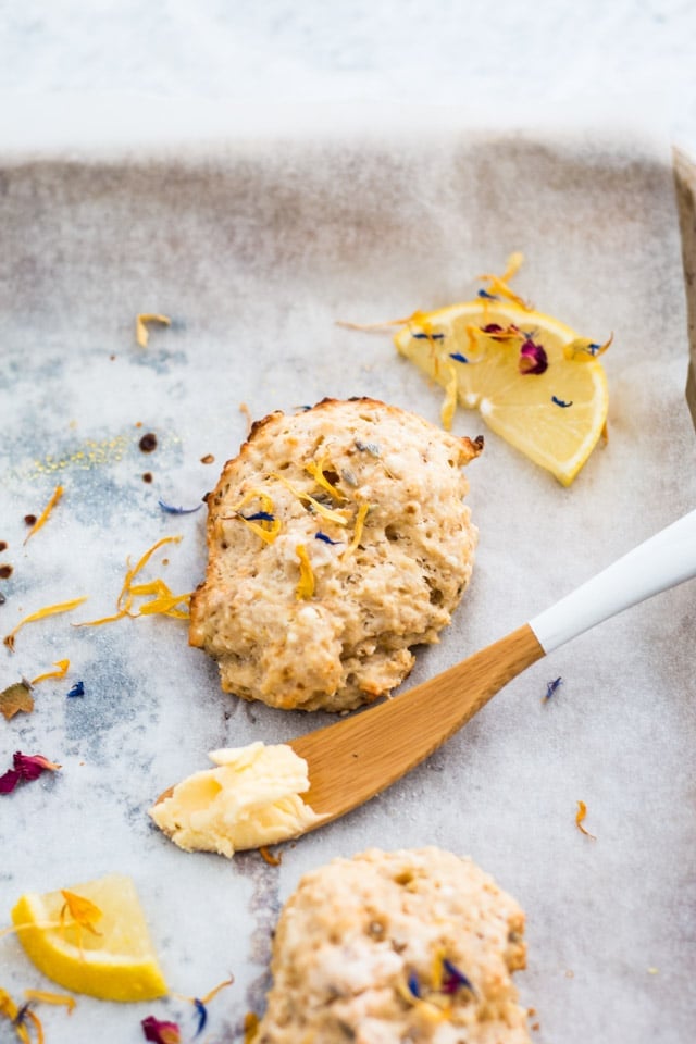 Overhead shot of a lemon and lavender scone on a baking tray and sprinkled with edible flowers and small lemon wedges