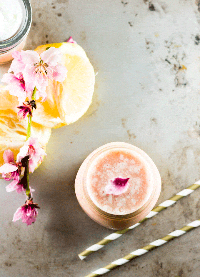 overhead shot of a pink Pineapple and Grapefruit Smoothie with fresh lemons and pink flowers scattered around the outside