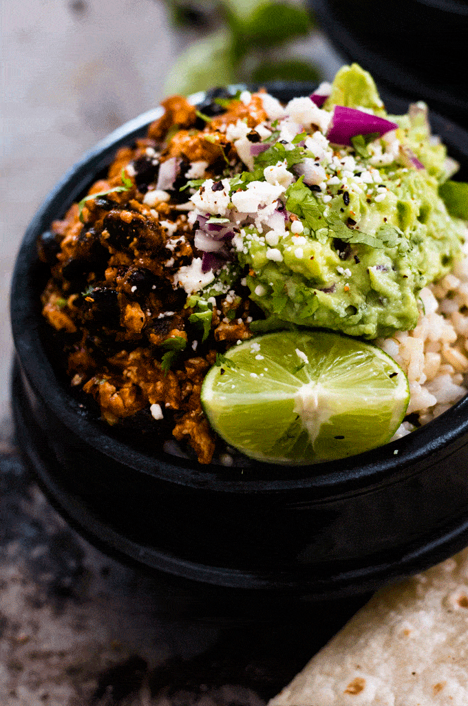 a tofu bowl topped with guacamole, red onion and lime wedges 