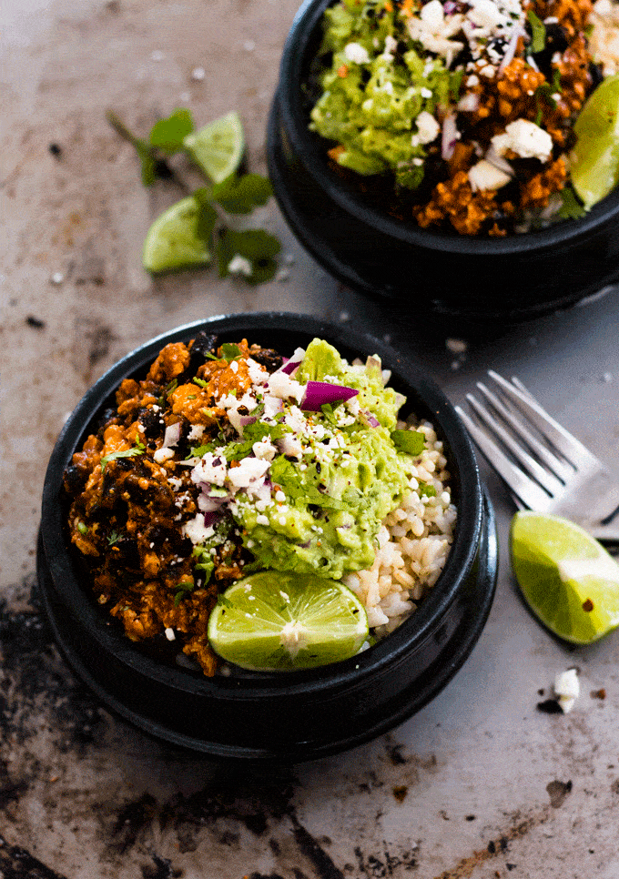 two black bowls filled with a vegetarian burrito mixture and topped with guacamole and lime wedges