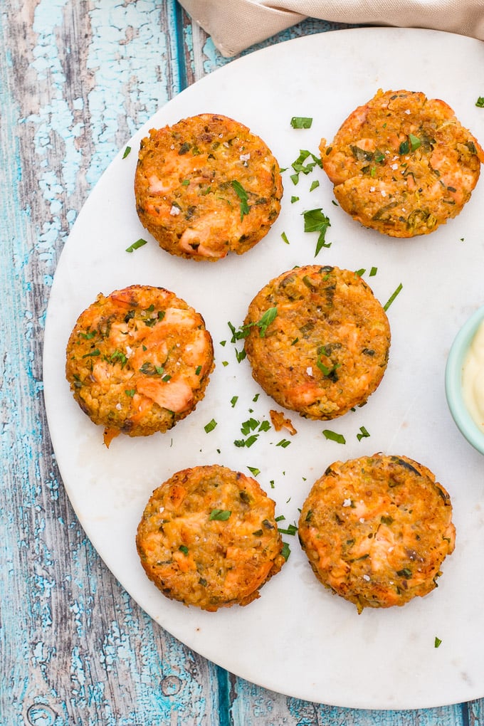 Quinoa and salmon burgers laid out on a white platter with a sprinkling of fresh parsley