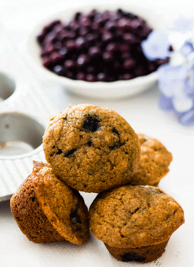 A stack of mini muffins with a bowl of blueberries in the background