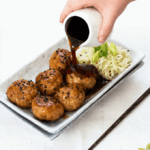 Sauce being poured over a platter of 6 pork meatballs served with noodles