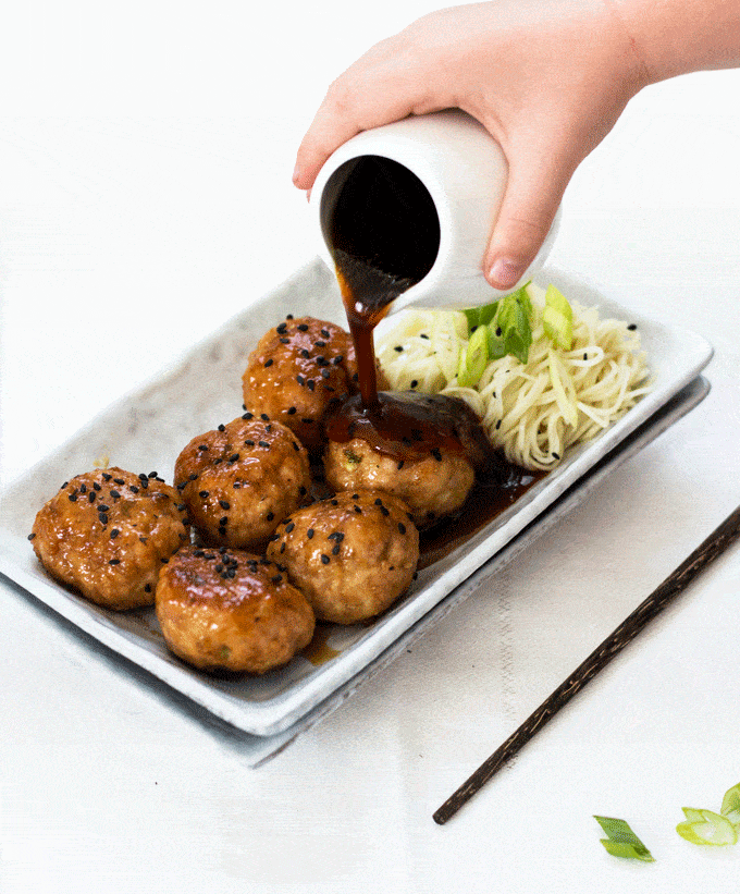 Sauce being poured over a platter of 6 pork meatballs served with noodles