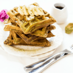 A stack of banana matcha waffles on a white plate, topped with fresh banana slices