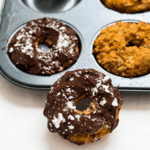 Chocolate covered pumpkin pie donuts resting against a donut tray