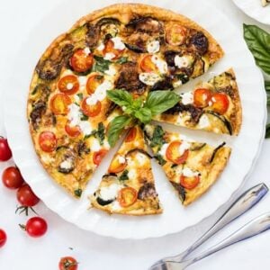 Overhead shot of a tomato and feta frittata served on a white plate and topped with fresh basil