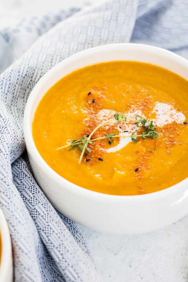 Close up shot of pumpkin and carrot soup served in a white bowl with pale blue and white linen