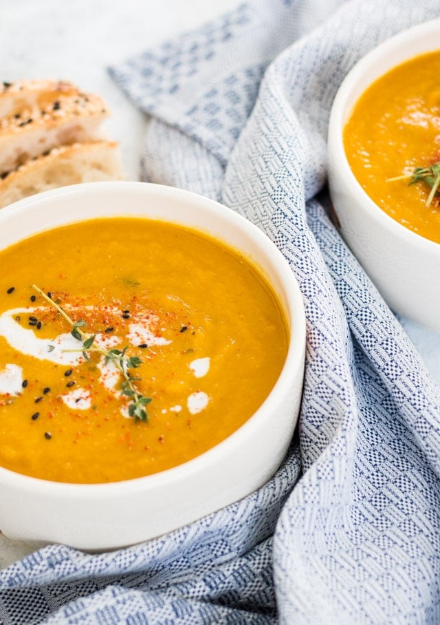 Pumpkin and Carrot Soup served in a white bowl and topped with some coconut milk and thyme with purple flowers