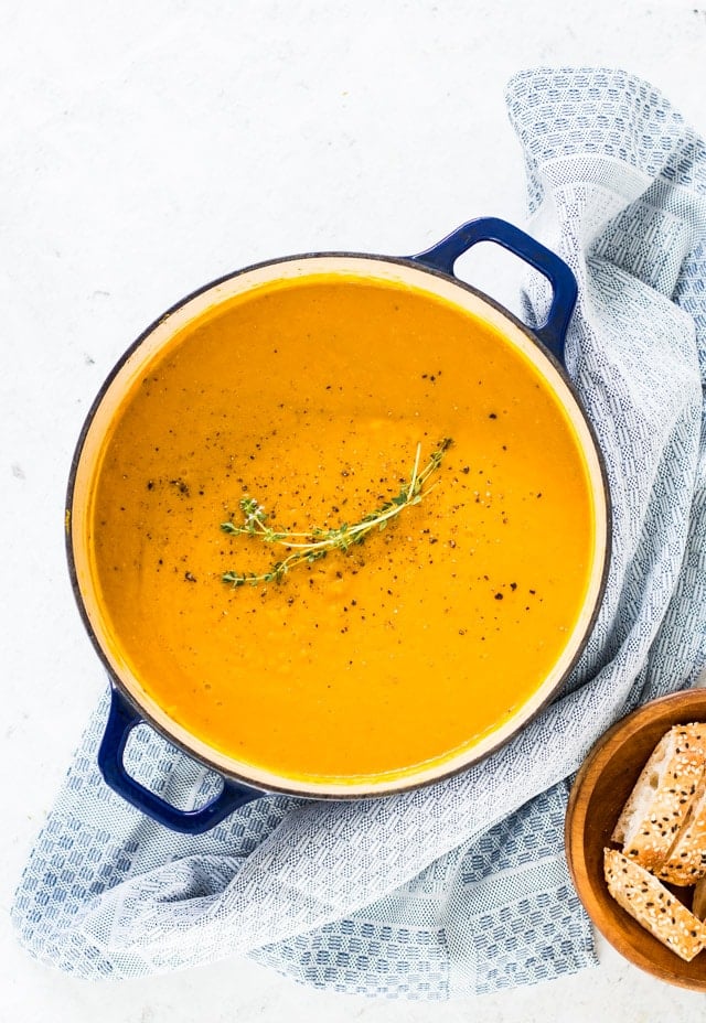 A big blue dutch oven with blended pumpkin and carrot soup topped with some fresh herbs