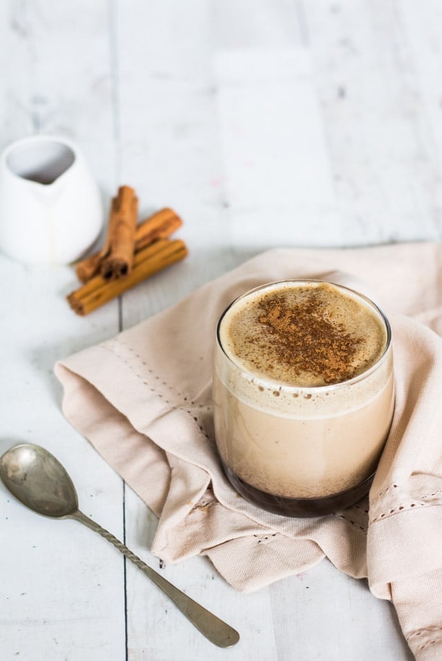 Green Tea Chai Spiced Latte served in a glass with maple syrup and cinnamon sticks in the background