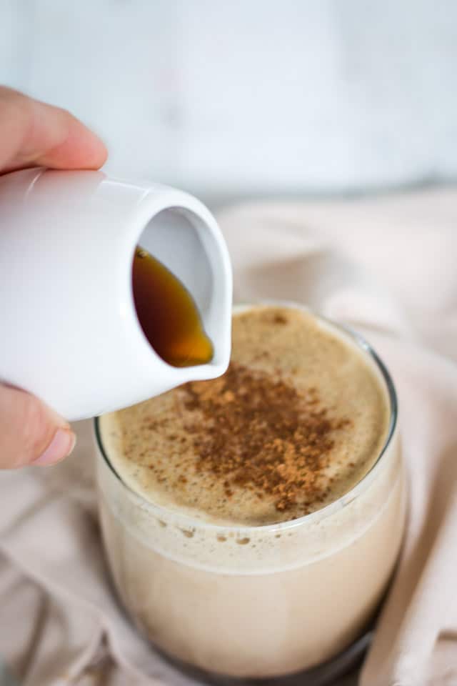 Maple syrup being poured from a small white jug into a green tea latte