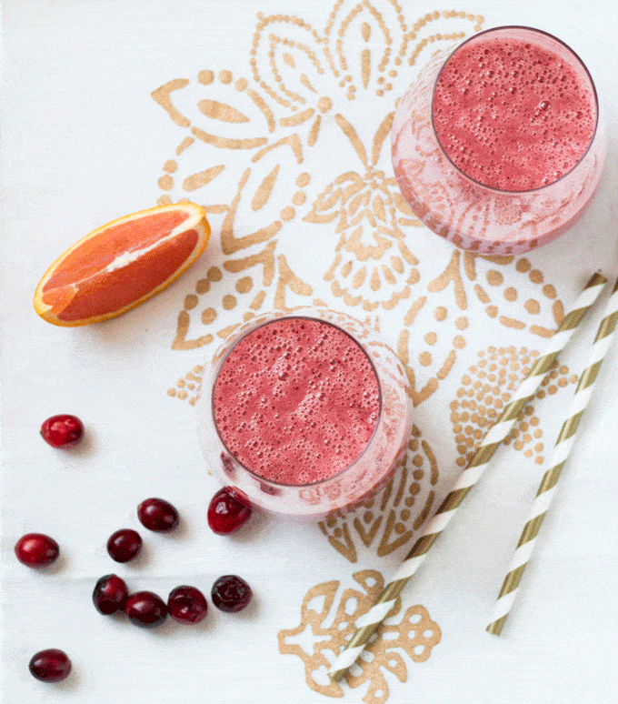 Cranberry smoothie served in a nice glass on a white and gold tablecloth with white and gold straws on the side