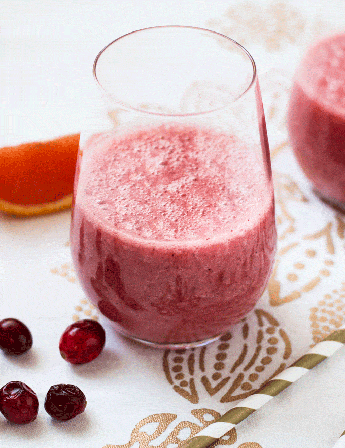 Up close shot of a pink smoothie in a nice glass with orange wedges in the background