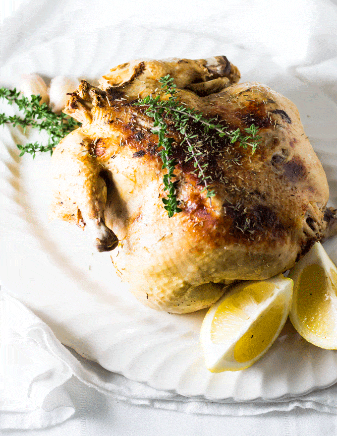 whole pressure cooker chicken served on a white serving platter with some fresh thyme and lemon wedges