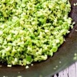 broccoli rice being cooked in a wok and stirred with a wooden spatula