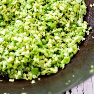 broccoli rice being cooked in a wok and stirred with a wooden spatula