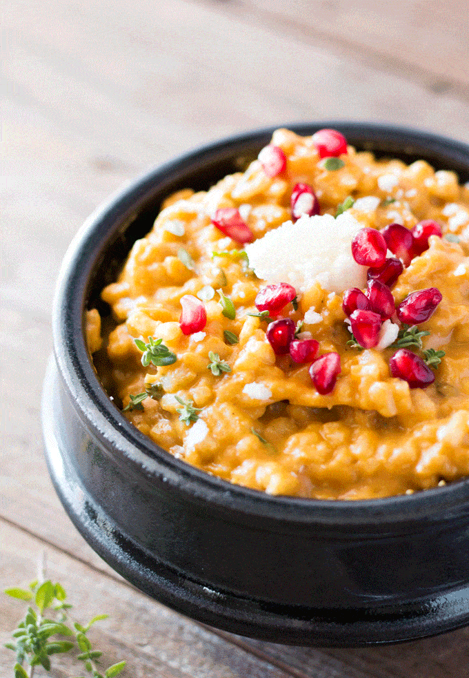 Up close shot of a pumpkin risotto served in a black bowl with a sprinkling of pomegranate and fresh goat's cheese on top