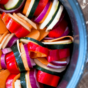 up close shot of colorful veggies layered in the bowl of a slow cooker to make ratatouille