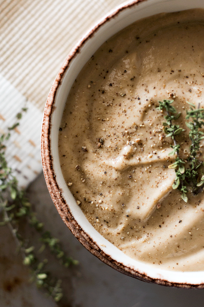 a creamy soup served in a beige bowl with sprigs of fresh thyme on top