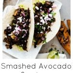 Mushroom and smashed avocado tacos on a steal background with a wooden spoon and limes surrounding