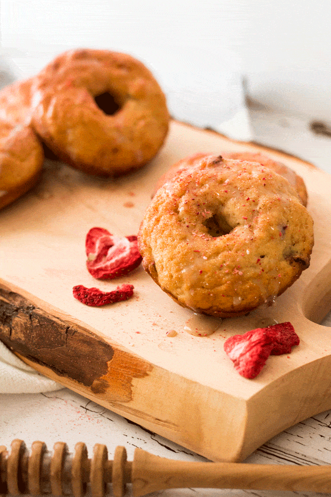 Up close shot of baked donuts on a wooden board surrounded by chopped freeze-dried strawberries