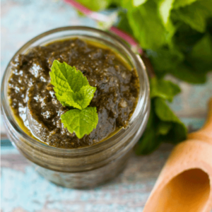 Mint Pesto in a glass jar with some fresh mint and a serving spoon in the background