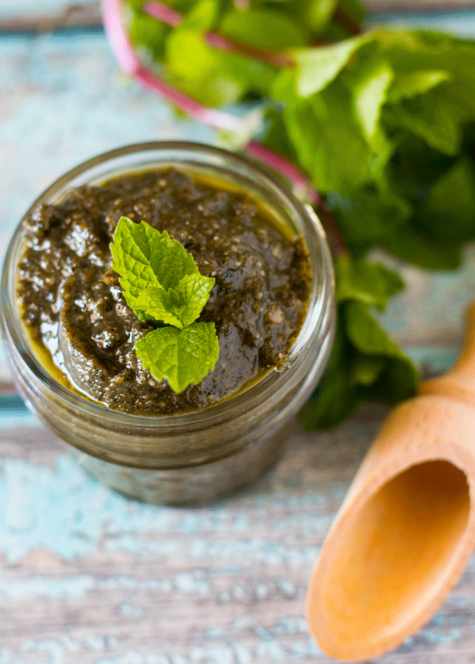 Mint Pesto in a glass jar with a small wooden spoon for serving and some fresh mint in the background