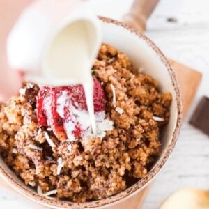 Chocolate covered strawberry quinoa breakfast in an off white bowl with milk being poured on top