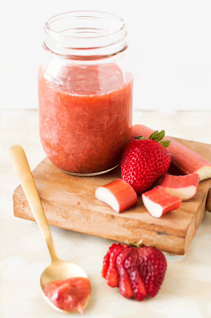 Strawberry Rhubarb Compote in a glass mason jar surrounded by chopped strawberries and rhubarb
