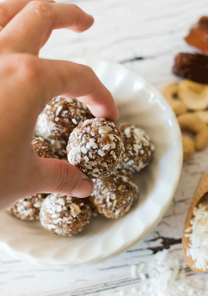 Easy No Bake Cashew and Coconut Date Balls being picked up out of a white bowl