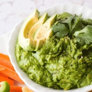 Green pea Guacamole in a white bowl with slices of fresh avocado on top