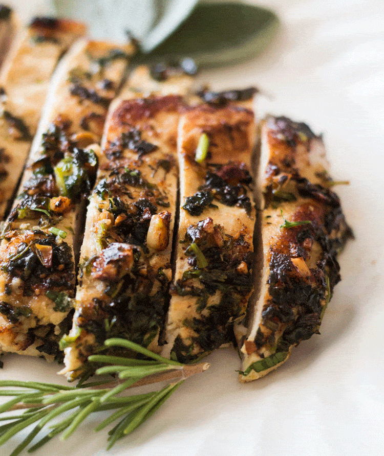 Macadamia Nut Chicken Breasts sliced and served with fresh herbs on a white platter plate