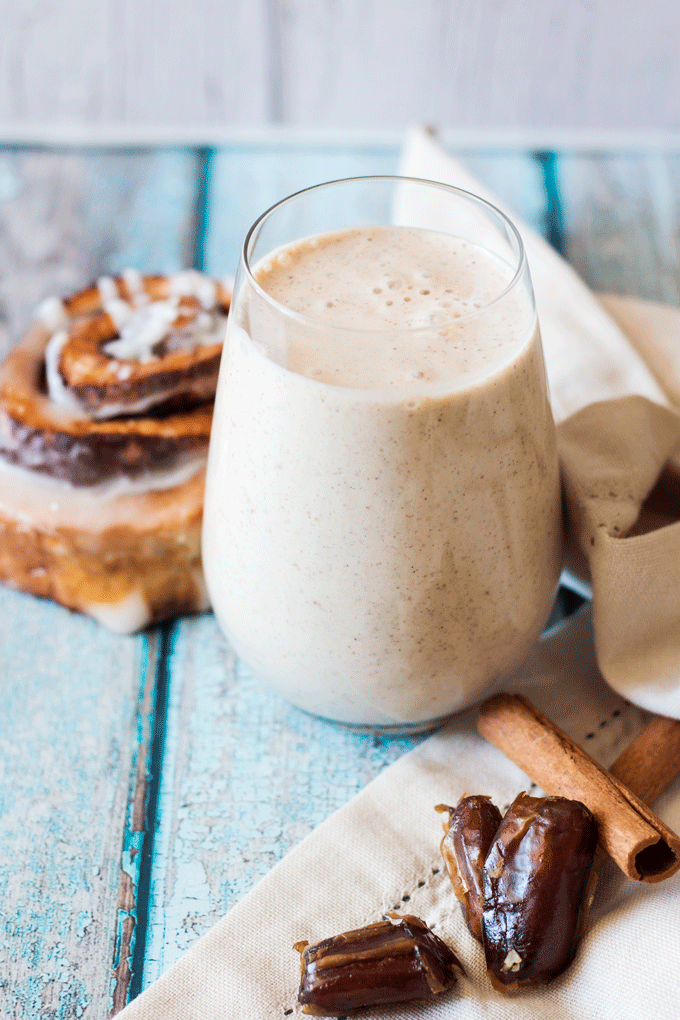 Banana Cinnamon Roll Smoothie with a cinnamon scroll, dates and cinnamon sticks in the background