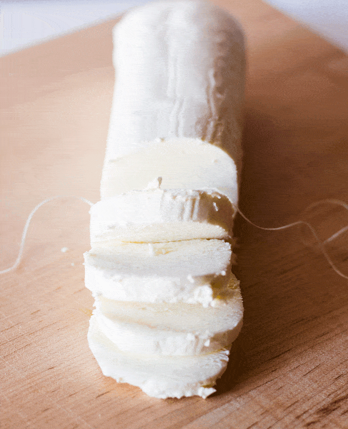 fresh goat cheese being cut for Marinated Goat Cheese Log with Fresh Garden Herbs