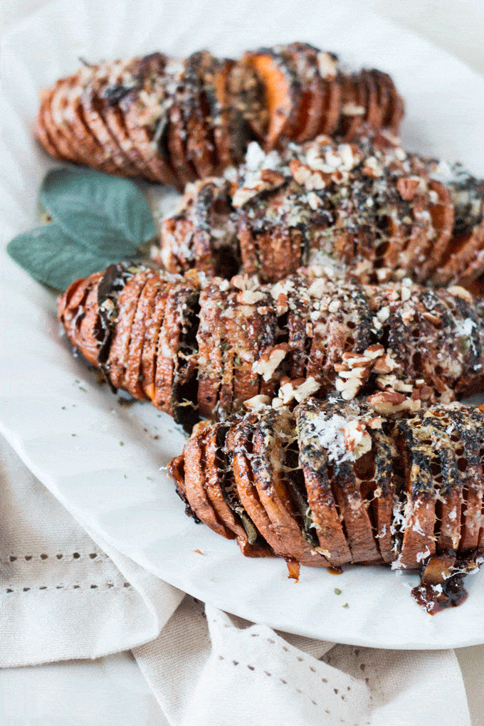 Completed Parmesan and Sage Hasselback Sweet Potatoes served on a white platter and topped with toasted pecans 