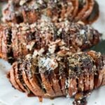 Hasselback Sweet Potatoes on a while plate and topped with parmesan and chopped pecans
