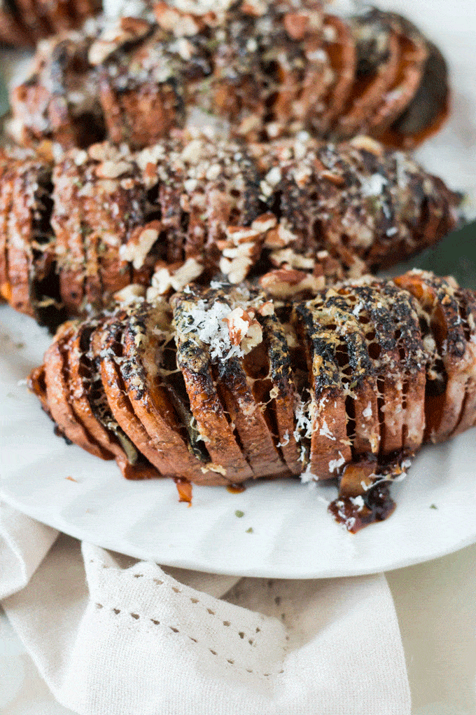 3 Parmesan and Sage Hasselback Sweet Potatoes on a white plate. Topped with parmesan and toasted walnuts