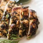 Sliced Sage and Macadamia Nut Chicken Breasts on a wooden board surrounded by sprigs of fresh rosemary