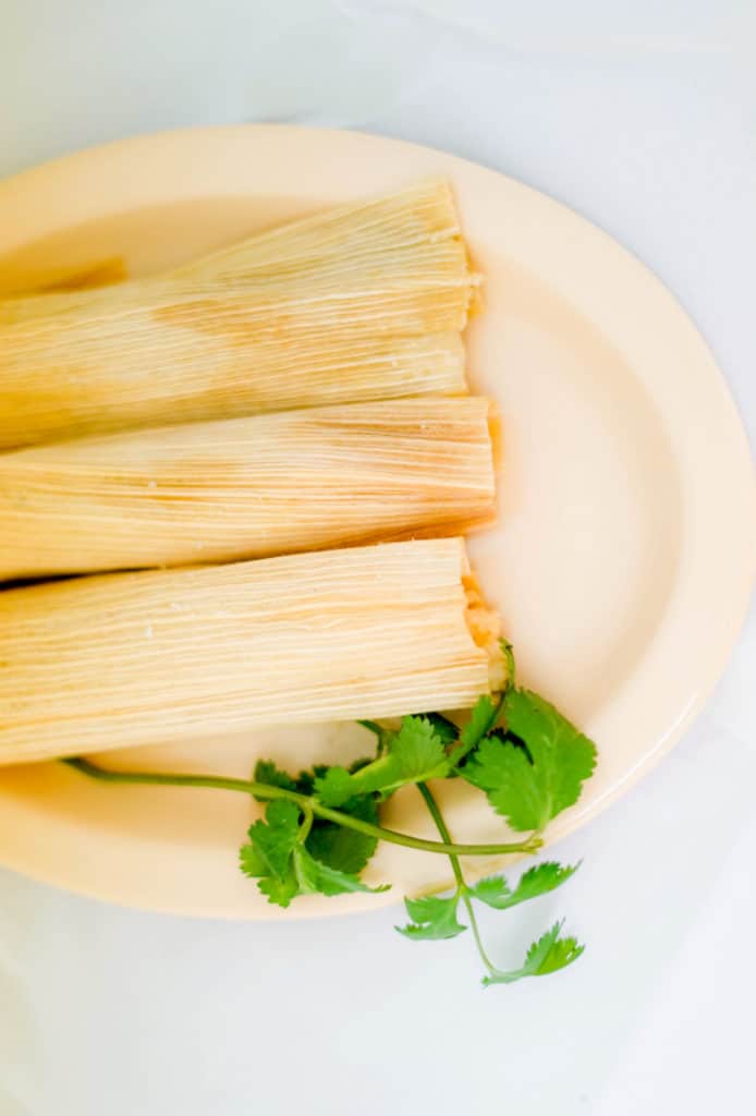 3 vegan tamales on a cream plate with some cilantro on the side