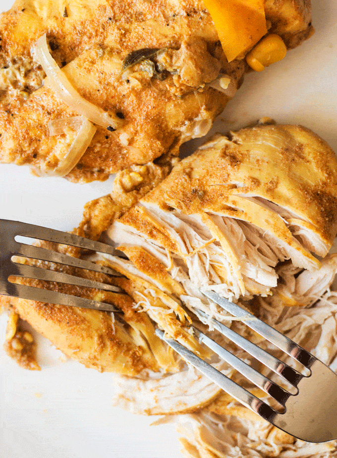 A cooked chicken breast being shredded with two forks