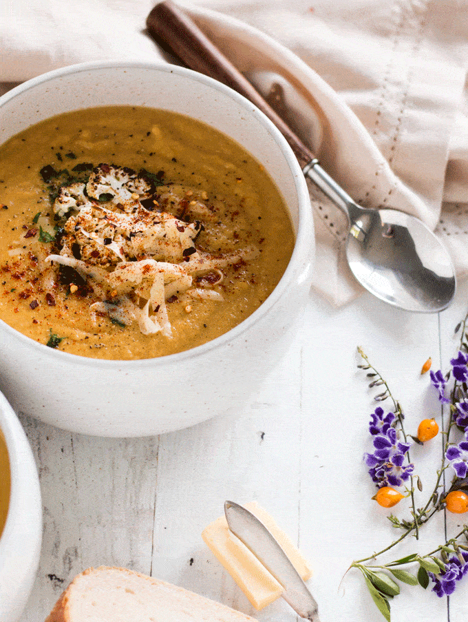 Cheesy Broccoli Cauliflower Soup served in a white bowl on a white wooden background