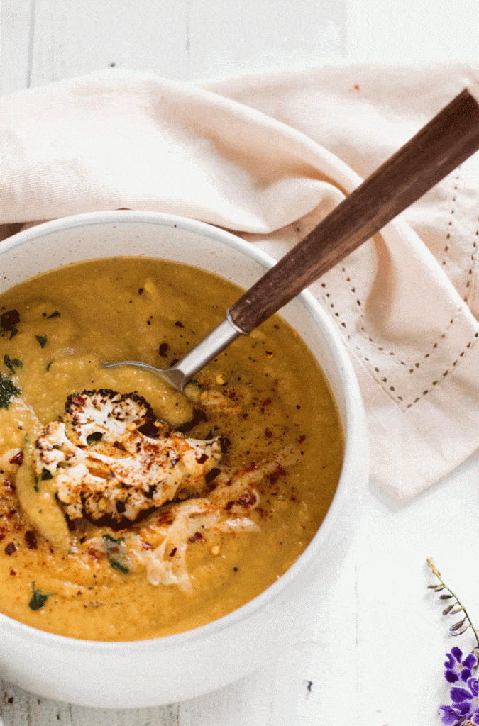 Cheesy Broccoli Cauliflower Soup with a wooden spoon taking some from the bowl