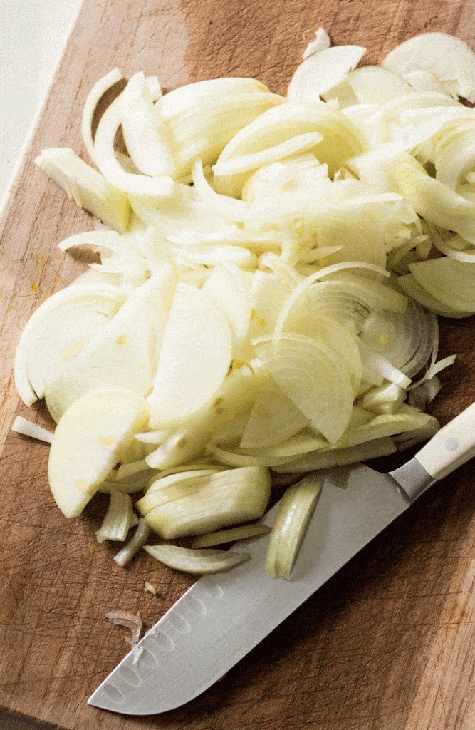 wooden chopping board with lots of thinly sliced onions and a sharp knife