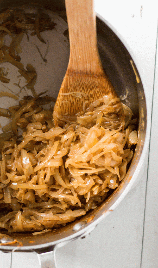 saucepan with Balsamic Caramelized Onions inside being stirred by a wooden spoon
